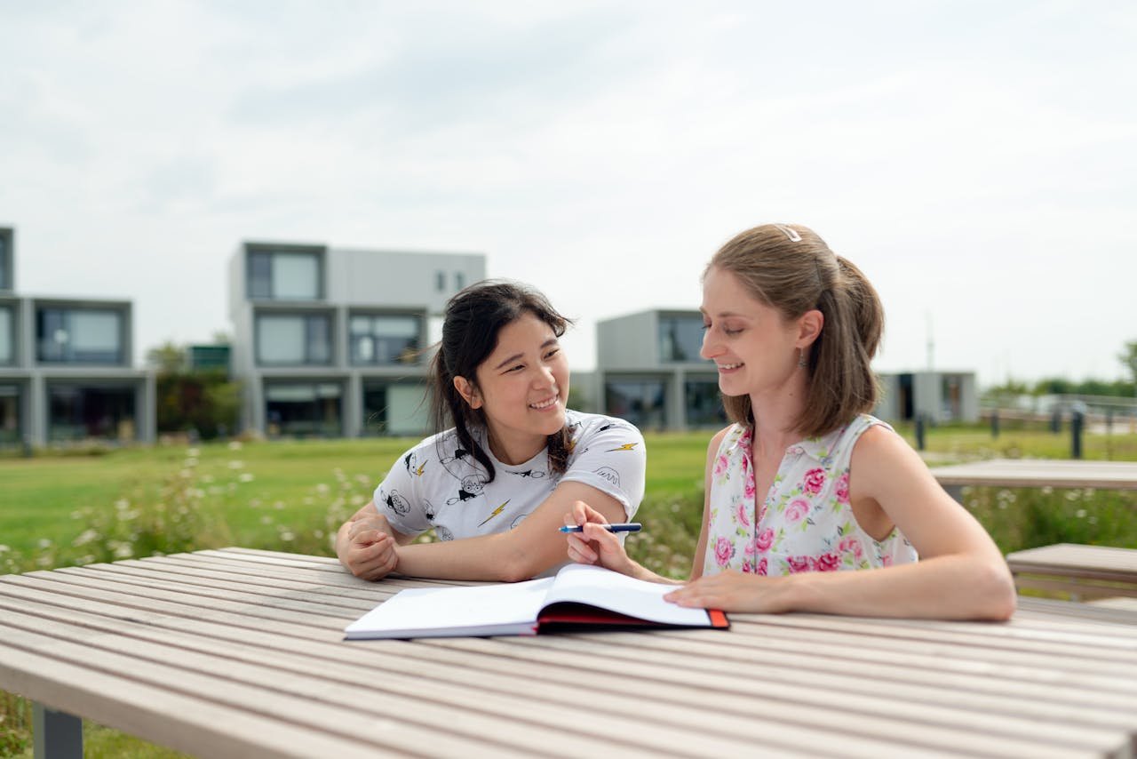 Two young women studying together outdoors on a modern campus, enjoying a sunny day.